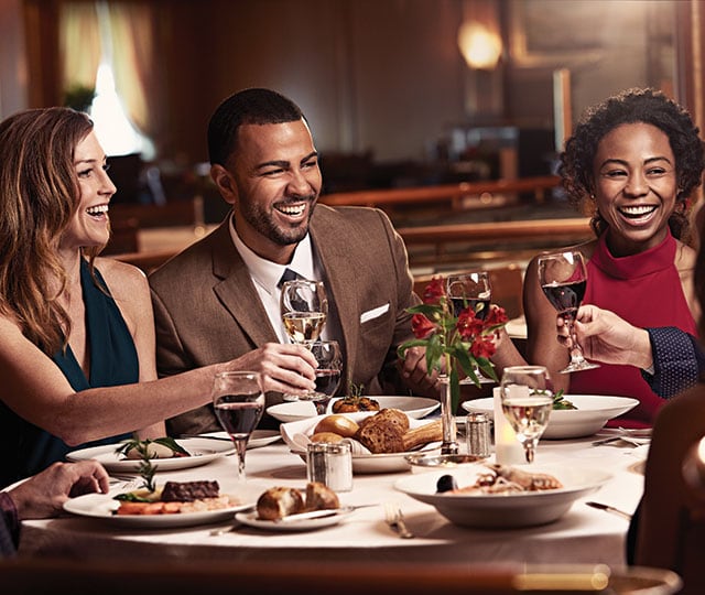 friends sitting around a dinner table, raising their glasses of wine for a toast