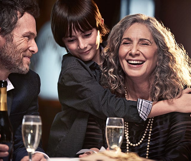 grandparents at dinner table with grandson inbetween them, giving grandmother a hug