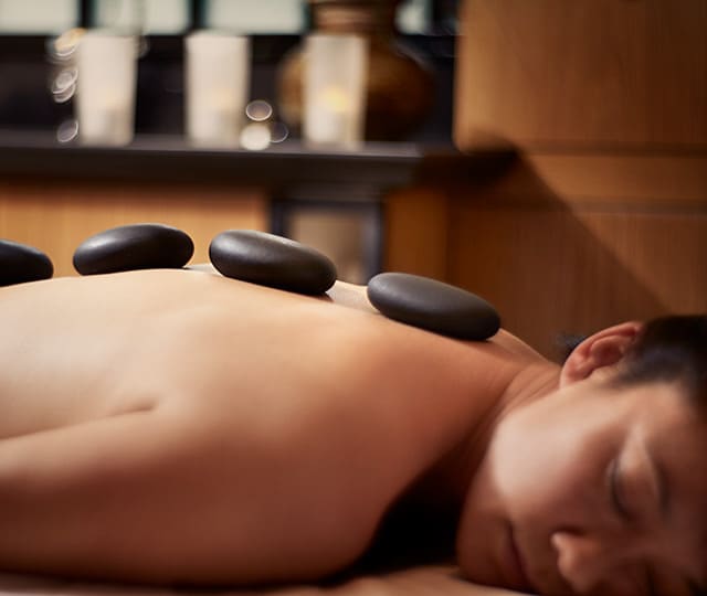 woman laying on massage table in spa relaxing while receiving hot stone massage