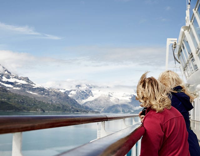 Two women lean against railing with mountains and glaciers in view