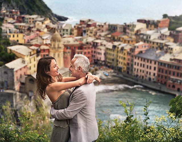 Couple embraces with seaside Italian village as the backdrop.