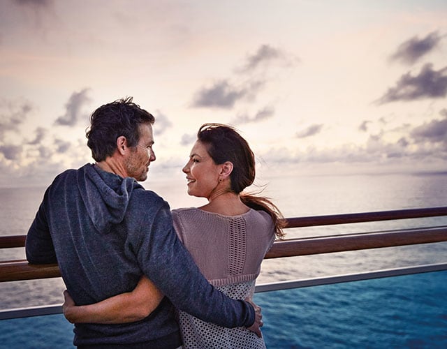 Couple embracing by railing, overlooking the ocean